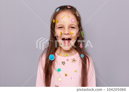 Indoor shot of excited extremely happy little brown haired little girl covered with stickers screaming with joyful expression, rejoicing posing isolated over gray background Indoor shot of excited extremely happy little brown haired little girl covered with stickers screaming with joyful expression, rejoicing posing isolated over gray background 104205060