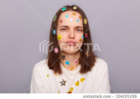 Indoor shot of sad stressed offended disappointed woman covered with funny stickers looking at camera with pout lips, being upset, posing isolated over gray background 104205289