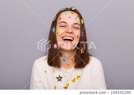 Horizontal shot of laughing joyful woman covered with funny stickers posing isolated over gray background, hearing funny joke, expressing positive emotions. Horizontal shot of laughing joyful woman covered with funny stickers posing isolated over gray background, hearing funny joke, expressing positive emotions. 104205290