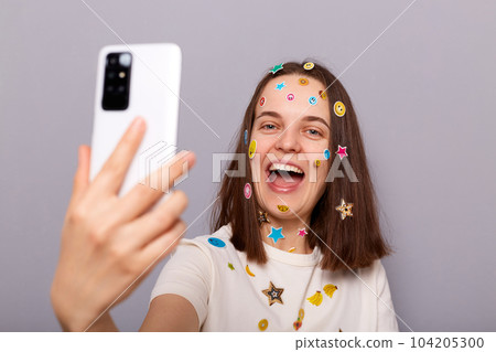 Photo of laughing woman blogger covered with funny stickers making selfie having video call broadcasting livestream posing isolated over gray background Photo of laughing woman blogger covered with funny stickers making selfie having video call broadcasting livestream posing isolated over gray background 104205300