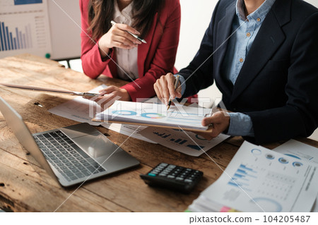 Team of two asian male and female business people working together discussing new financial graph data on office table with laptop and digital tablet. 104205487