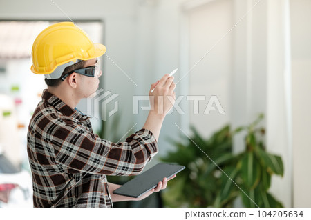 Engineers man standing in front of windows. Engineer man point his hand to building outside. Engineering and construction concept. Engineers man standing in front of windows. Engineer man point his hand to building outside. Engineering and construction concept. 104205634