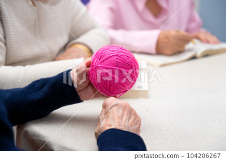 Close up of an old woman hands as she winds a woolen thread at nursing home. Close up of an old woman hands as she winds a woolen thread at nursing home. 104206267