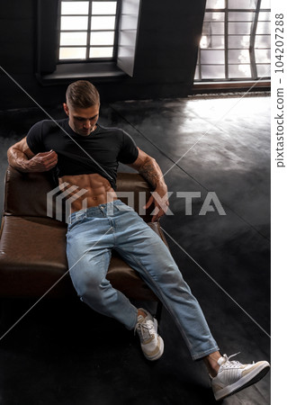 Athletic young man holding up black t-shirt and shows six pack abs Athletic young man holding up black t-shirt and shows six pack abs 104207288