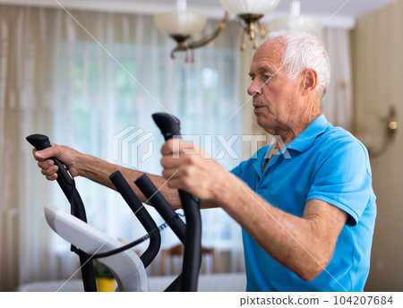 Old man using elliptic trainer at home 104207684