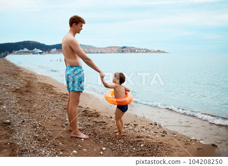 The son calls his father to swim in the sea. Child with inflatable ring. Summer vacation concept 104208250