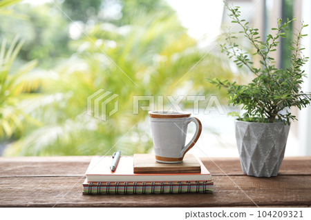 Vintage ceramic coffee cup and notebooks and plant pot on brown wooden table 104209321