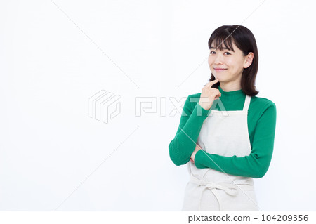 Housewife in her thirties wearing an apron thinking with a smile in front of a white background Housewife in her thirties wearing an apron thinking with a smile in front of a white background 104209356