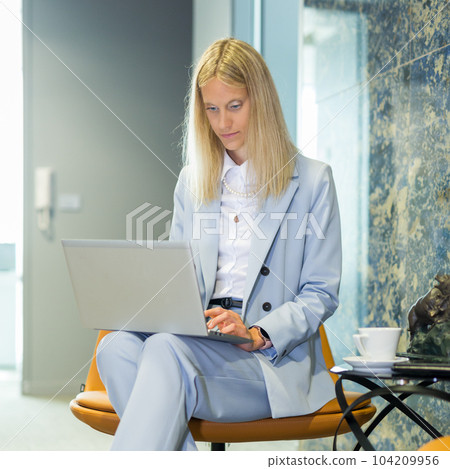 Beautiful business woman sitting at the table working on a laptop. Stylish woman in the modern office environment Beautiful business woman sitting at the table working on a laptop. Stylish woman in the modern office environment 104209956