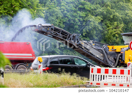 Asphalt milling and grinding machine at road repair and construction site throwing shredded old bitumen in big industrial heavy dumper tipper truck for recycling. Highway renewal with heavy machinery Asphalt milling and grinding machine at road repair and construction site throwing shredded old bitumen in big industrial heavy dumper tipper truck for recycling. Highway renewal with heavy machinery 104210147