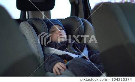A small child sleeps in a car seat in a parking lot. Boy in a sweatshirt and hat. A small child sleeps in a car seat in a parking lot. Boy in a sweatshirt and hat. 104210374