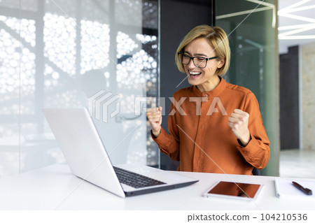 Successful businesswoman inside the office is satisfied with the results of the achievement, the employee received a good completed technical task, holds her hands up in a gesture of triumph Successful businesswoman inside the office is satisfied with the results of the achievement, the employee received a good completed technical task, holds her hands up in a gesture of triumph 104210536