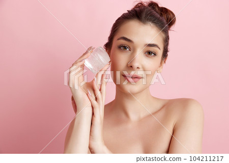 Young beautiful woman taking care after her perfect skin with ice cube against pink studio background. refreshment and anti-wrinkle care 104211217