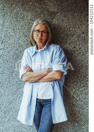 mature lady with gray hair, standing near wall. Lady's confident demeanor, reflecting her wisdom and experience. She exudes air of elegance and sophistication, with stylish appearance and poised 104212512