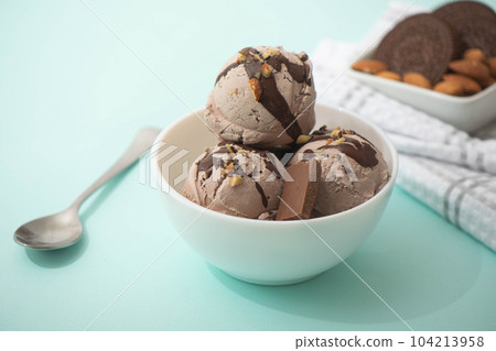 Chocolate ice cream decorated with nuts and chocolate icing, in a white bowl, blue background. Summer homemade cooling desserts Chocolate ice cream decorated with nuts and chocolate icing, in a white bowl, blue background. Summer homemade cooling desserts 104213958