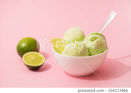 Ice cream with lime flavor and slices of fresh lime in a white bowl, pink background, copy space. Summer cooling desserts, 104213966