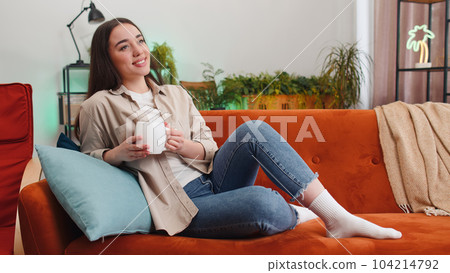 Attractive smiling young woman drinking a cup of coffee or herbal tea relaxing resting at home couch Attractive smiling young woman drinking a cup of coffee or herbal tea relaxing resting at home couch 104214792