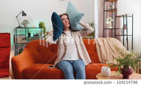 Repair work at neighbours concept, irritated woman at home cover ears with pillows annoyed by noise Repair work at neighbours concept, irritated woman at home cover ears with pillows annoyed by noise 104214796