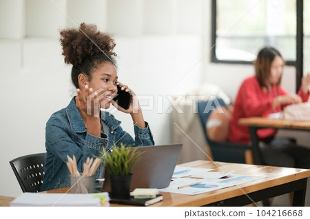Smart African women working in beautiful office, working on Laptop, use the phone, talking on the cellphone.  104216668