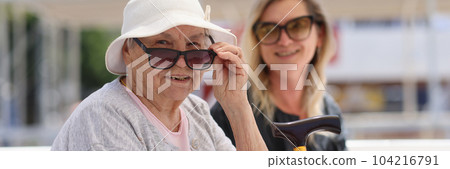 Old granny with cane sitting on bench with young woman 104216791