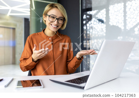 Happy businesswoman working in modern office using laptop for video call and online meeting with fellow employees, woman smiling and having fun giving a presentation. Happy businesswoman working in modern office using laptop for video call and online meeting with fellow employees, woman smiling and having fun giving a presentation. 104217363