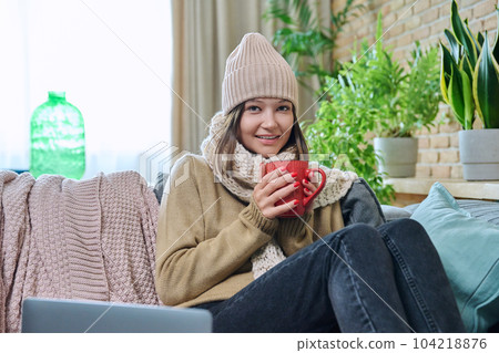 Young woman in sweater hat sitting at home, basking with cup of hot drink Young woman in sweater hat sitting at home, basking with cup of hot drink 104218876
