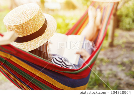 Young woman reading book while lying in comfortable hammock at green garden Young woman reading book while lying in comfortable hammock at green garden 104218964