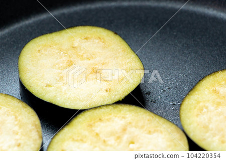 A cooking scene where eggplants are cut into round slices and baked in a frying pan. A cooking scene where eggplants are cut into round slices and baked in a frying pan. 104220354