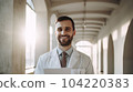 Hospital. Health care. Portrait of young smiling 30-year-old bearded caucasian man doctor wearing white medical coat with stethoscope around his neck, looking at camera. Hospital Corridor, AI 104220383
