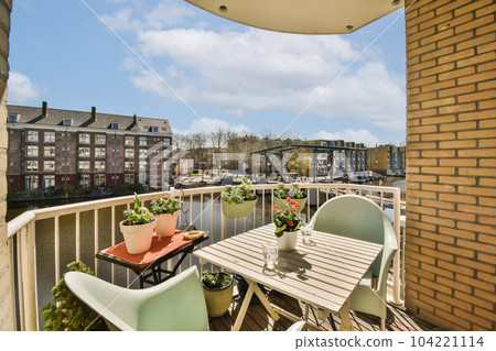 some chairs and tables on a balcony with buildings in the backgrunde area behind them, there is a blue sky 104221114