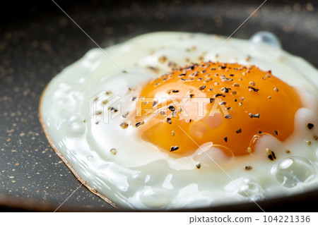 A cooking scene where fried eggs are baked in a frying pan. (coarsely ground black pepper) A cooking scene where fried eggs are baked in a frying pan. (coarsely ground black pepper) 104221336