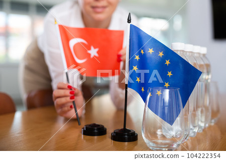 Young woman puts Turkey and EU flags on table in office 104222354