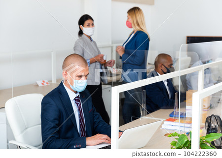 Confident manager in medical mask working with laptop in office 104222360