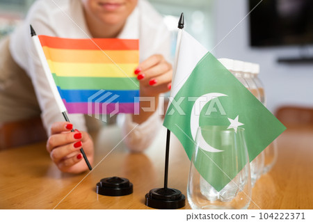 Young woman putting LGBT and Pakistani flags on table in office Young woman putting LGBT and Pakistani flags on table in office 104222371