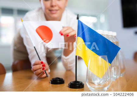 Unrecognizable girl sets midget flags of Ukraine and Japan before international negotiations 104222406