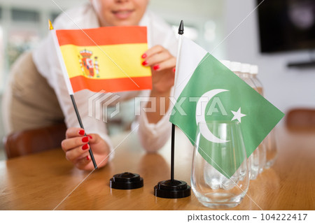 Little flag of Pakistan on table and flag of Spain put next to it by young woman Little flag of Pakistan on table and flag of Spain put next to it by young woman 104222417