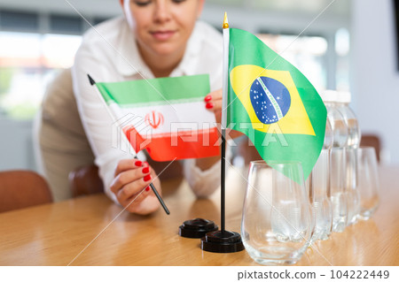 Little flag of Brazil on table and flag of Iran put next to it by young woman Little flag of Brazil on table and flag of Iran put next to it by young woman 104222449