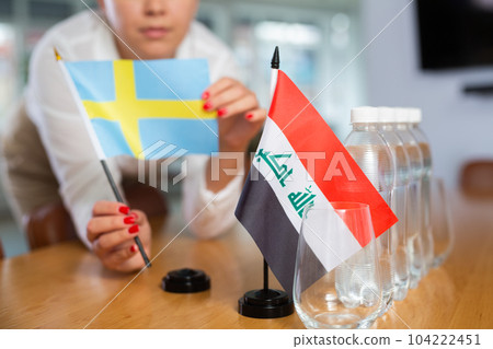Employee of delegation prepares negotiating table - sets up flag of Iraq and Sweden 104222451