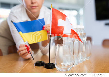 Little flag of Switzerland on table and flag of Ukraine put next to it by young woman 104222536