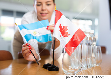 Young woman putting flags of Argentina and Canada on table in office Young woman putting flags of Argentina and Canada on table in office 104222596