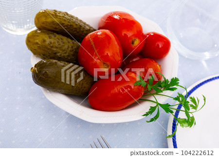 Pickled cucumbers and tomatoes served on plate with parsley 104222612