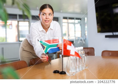 Positive young woman putting little flag of South Africa on table next to the flag of Switzerland 104222776