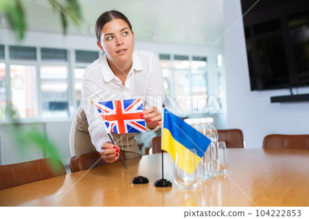 Young lady sets miniatures Ukrainian and British flags for international negotiations 104222853