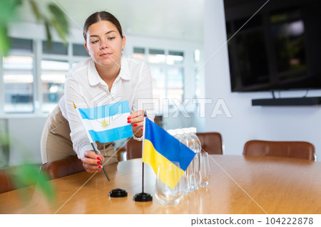 Female office coordinator placing flags of Ukraine and Argentina on table 104222878