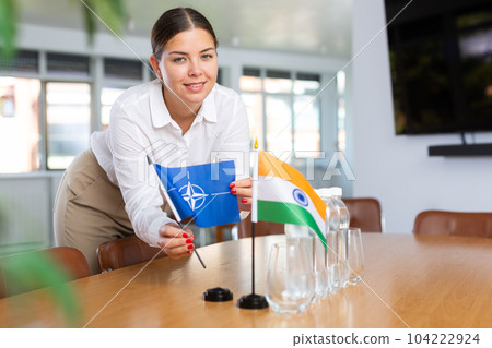 Woman secretary prepares an office for negotiations - she places flags of NATO (OTAN) and India table 104222924