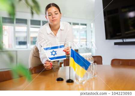 Young lady sets miniatures flags of Ukraine and Israel for international negotiations 104223093