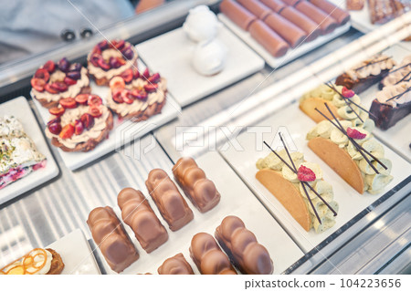 A variety of cakes covered with chocolate and decorated with pistachio mousse. A showcase in a pastry shop with delicious desserts with fresh berries and cream. Delicious pastries in the coffee shop. A variety of cakes covered with chocolate and decorated with pistachio mousse. A showcase in a pastry shop with delicious desserts with fresh berries and cream. Delicious pastries in the coffee shop. 104223656