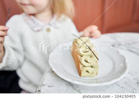 selective focus a child is sitting at a table in a cafe and trying a delicious dessert. a cute little girl eats dessert with pistachio cream in a cafe. Children's cafe. 104230405
