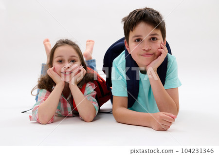 Smart school children, first grader - Caucasian little kid girl 6 years old and Hispanic teenage boy, lying on belly, smiling looking at camera, isolated on white background. Back to school concept 104231346