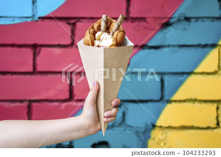 Street food dessert Belgian waffles in hand on a colored wall background. Sweets, street food 104233293